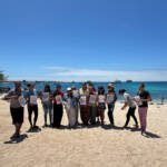 Foto grupal de guardianas azules mostrando carteles en el taller de liderazgo, género y empoderamiento emocional en la playa, en San Cristóbal